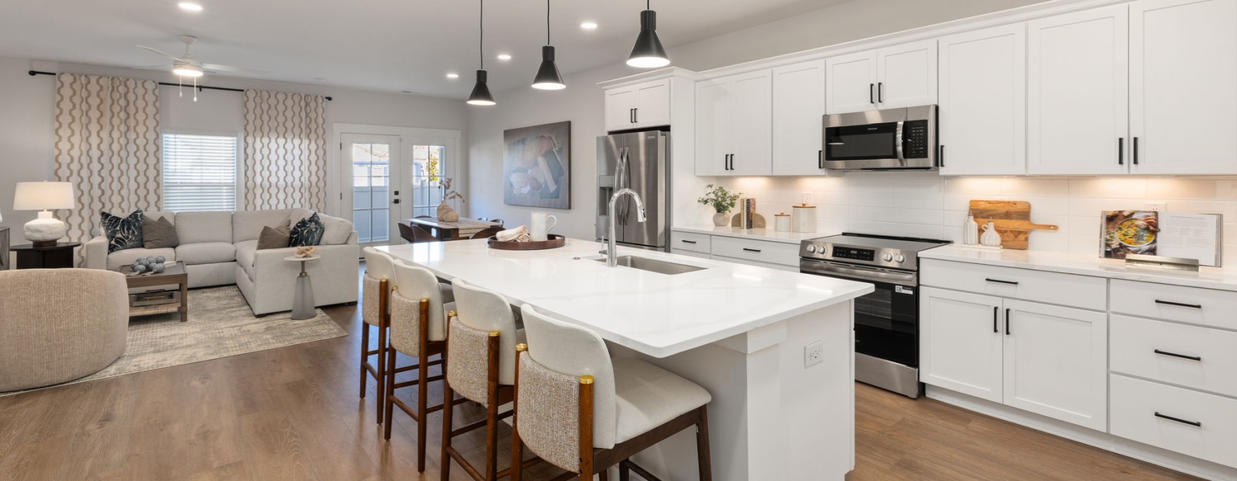 Open kitchen and living area at Oaks at Wendell with white cabinets, stainless steel appliances, and an island with bar seating.
