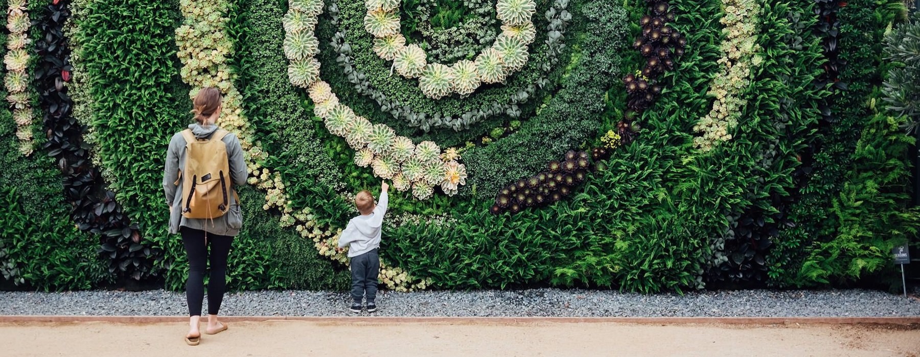 mother and child standing in front of a mural made of plants
